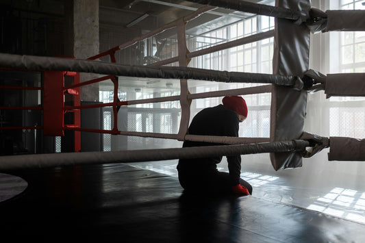 A boxer sits alone in the corner of a boxing ring, head lowered in reflection, capturing the nerves and anticipation before a first time sparring boxing session.
