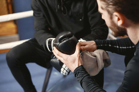 A coach helping a boxer adjust their gloves before a match, symbolizing the use of gear as a pre-fight ritual to enhance boxing IQ, improve ring IQ boxing, and build focus before stepping into the ring.
