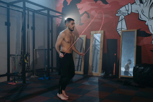 A shirtless boxer skips rope barefoot in a gym, focused on his form and rhythm, highlighting the role of skipping and jump rope workouts for boxers’ conditioning and footwork.
