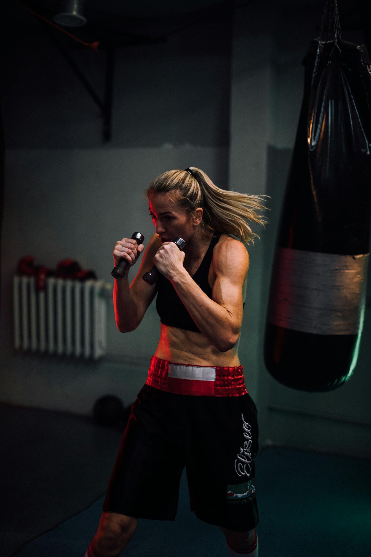 Female boxer training with dumbbells next to a heavy bag, showcasing dedication and boxing workout equipment aligned with the Fereli Code ethos.