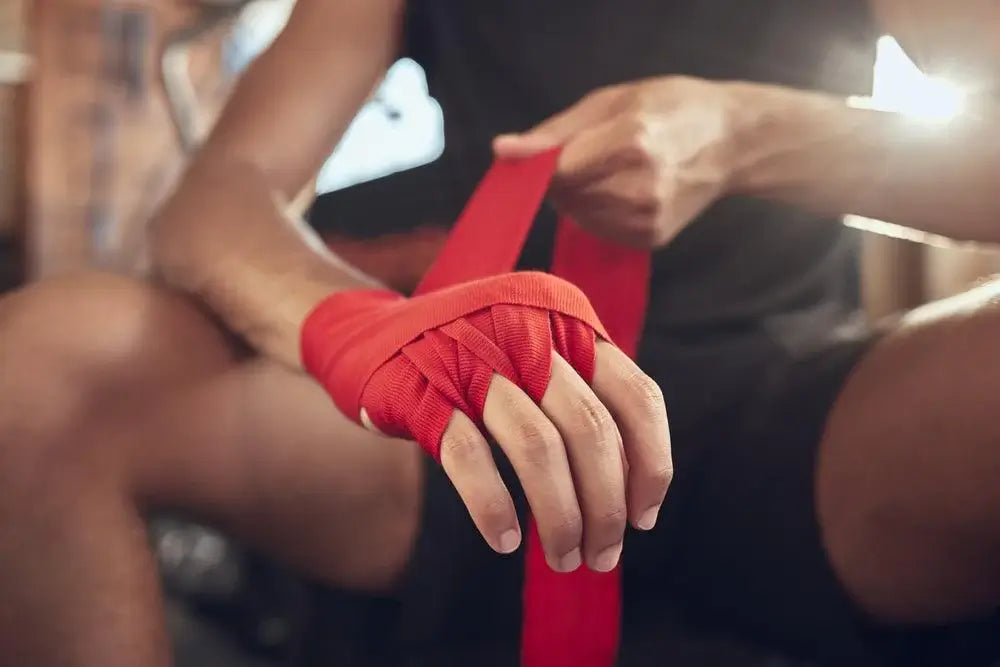 Close-up of a boxer wrapping red hand wraps around their knuckles and wrist before training, demonstrating proper hand wrapping technique for boxing support and protection.