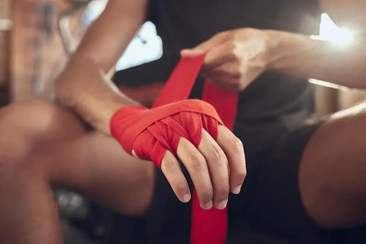 Close-up of a boxer wrapping red hand wraps around their knuckles and wrist before training, demonstrating proper hand wrapping technique for boxing support and protection.