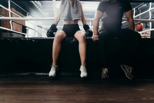 Boxers sitting on the ring apron wearing boxing gloves after training, illustrating different boxing glove padding types and recovery between rounds