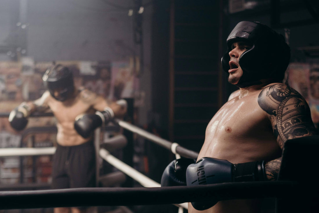 Two exhausted boxers in headgear resting on the ropes between rounds during sparring, illustrating the importance of stamina and endurance in boxing.