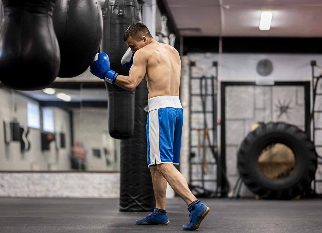 Boxer wearing blue gloves training on a heavy bag in a gym, demonstrating boxing glove weight and bag work practice.