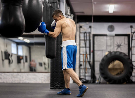 Boxer wearing blue gloves training on a heavy bag in a gym, demonstrating boxing glove weight and bag work practice.