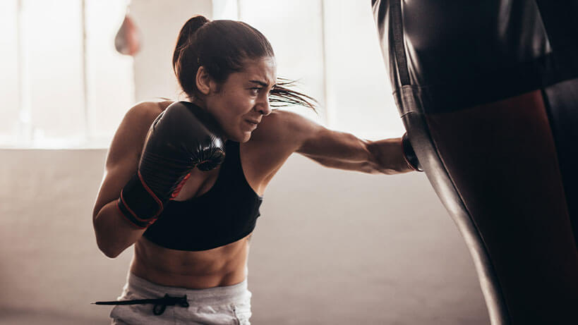 Female boxer punching a heavy bag during training, showing repeated impact that can cause boxing gloves to lose protection over time