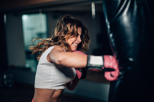 Woman punching a heavy bag with pink boxing gloves, representing focus, strength, and the importance of injury prevention in boxing training.