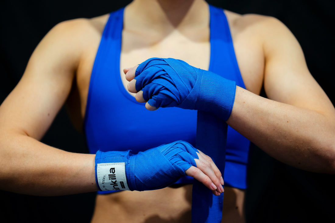 Close-up of a woman in a blue sports bra wrapping her hands with blue boxing wraps, preparing for a boxing fitness workout.