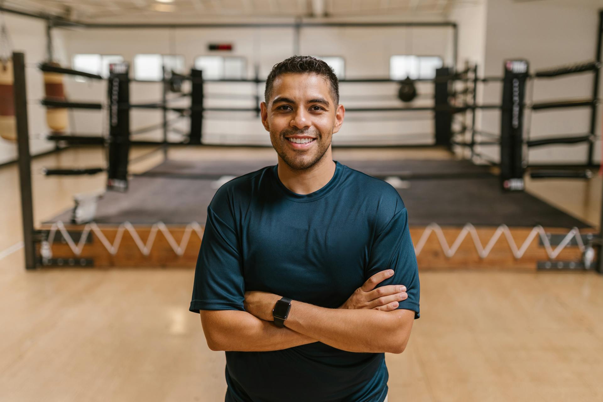 Experienced boxing coach at a top fighting shop gym, standing confidently in front of the ring where real fighters train.